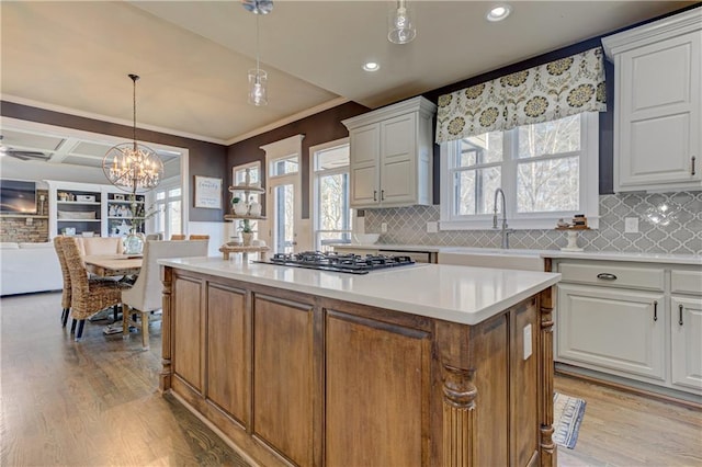 kitchen with light wood-style flooring, a sink, white cabinetry, a kitchen island, and stainless steel gas stovetop