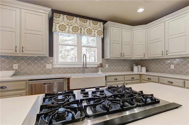 kitchen featuring tasteful backsplash, light countertops, stainless steel dishwasher, a sink, and black gas stovetop