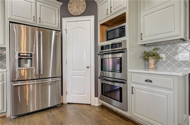 kitchen featuring light countertops, backsplash, appliances with stainless steel finishes, dark wood-type flooring, and white cabinetry