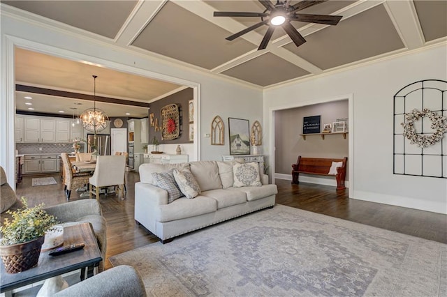 living area featuring baseboards, coffered ceiling, ornamental molding, dark wood-type flooring, and ceiling fan with notable chandelier