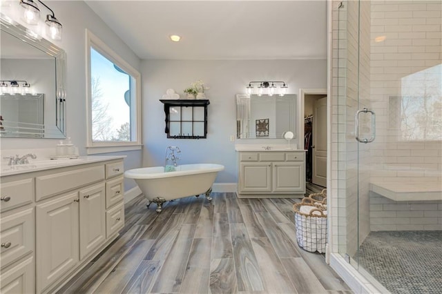 bathroom with wood finish floors, a soaking tub, a sink, a shower stall, and baseboards