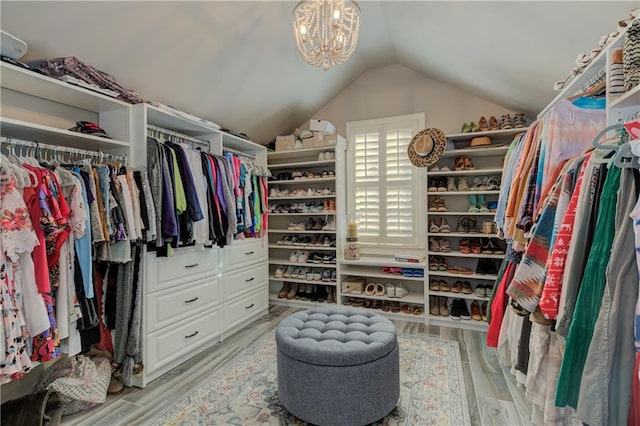 spacious closet with light wood-style floors, vaulted ceiling, and an inviting chandelier