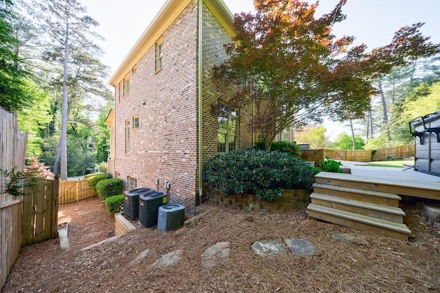 view of side of property featuring brick siding, central AC, a fenced backyard, and a wooden deck