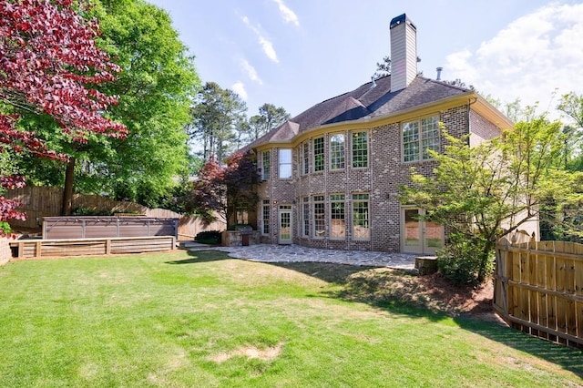 back of house with a chimney, a fenced backyard, a yard, french doors, and brick siding