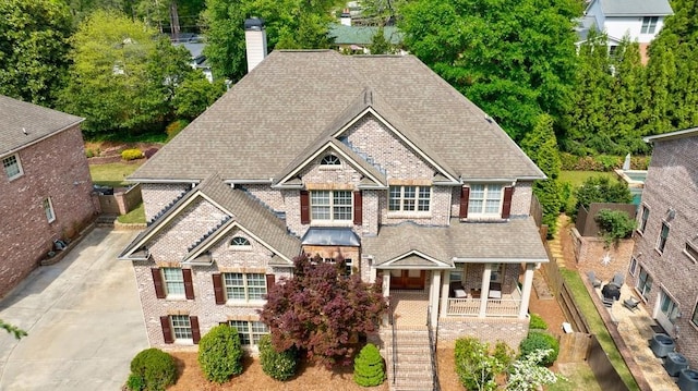 craftsman house with central air condition unit, covered porch, brick siding, a shingled roof, and stairway