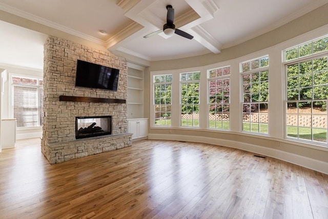 unfurnished living room with a ceiling fan, hardwood / wood-style floors, beamed ceiling, a fireplace, and ornamental molding