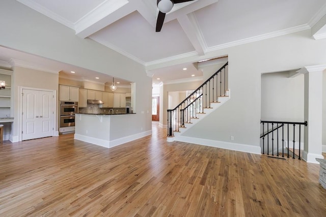 unfurnished living room with light wood finished floors, ornamental molding, beam ceiling, baseboards, and stairs