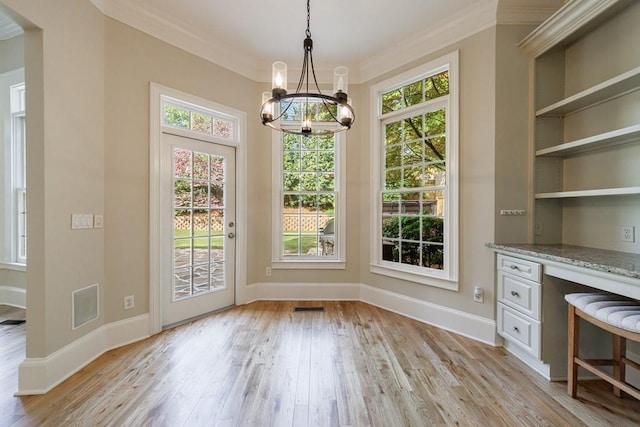 unfurnished dining area with built in study area, visible vents, light wood-type flooring, crown molding, and a chandelier