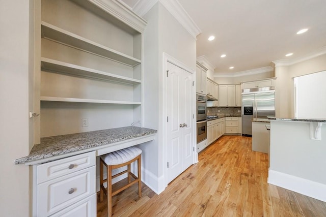 kitchen with built in desk, a breakfast bar, stainless steel appliances, ornamental molding, and light stone countertops