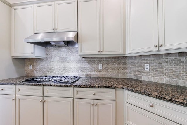 kitchen with dark stone counters, decorative backsplash, under cabinet range hood, and white cabinets