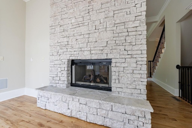 room details featuring baseboards, crown molding, wood finished floors, and a stone fireplace
