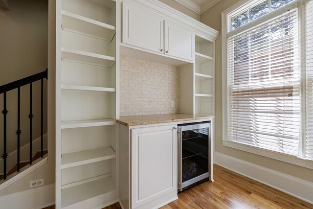 bar with beverage cooler, a bar, light wood-type flooring, baseboards, and decorative backsplash