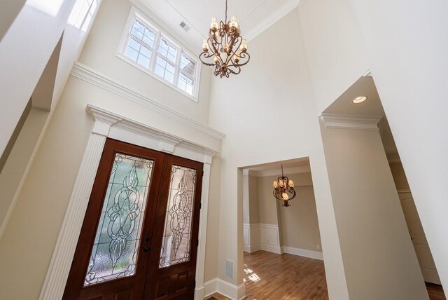 foyer featuring a towering ceiling, an inviting chandelier, wood finished floors, french doors, and baseboards