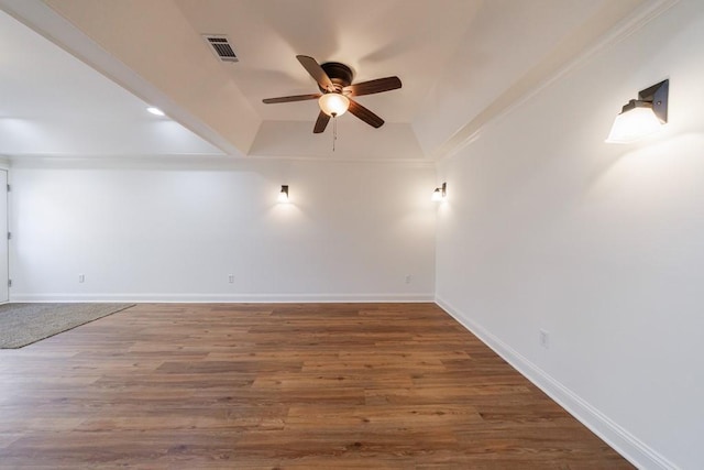 empty room featuring a tray ceiling, wood finished floors, a ceiling fan, and baseboards