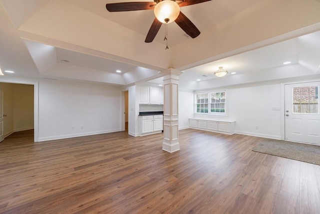 unfurnished living room with decorative columns, baseboards, wood finished floors, ceiling fan, and a raised ceiling