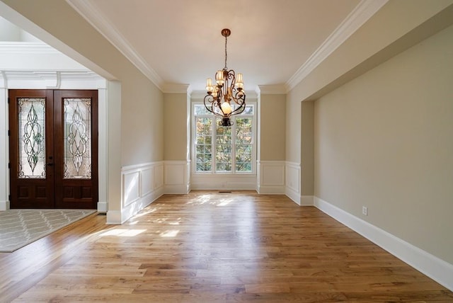 foyer entrance featuring wainscoting, ornamental molding, a notable chandelier, and wood finished floors