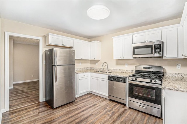 kitchen with light stone countertops, appliances with stainless steel finishes, white cabinetry, sink, and dark wood-type flooring