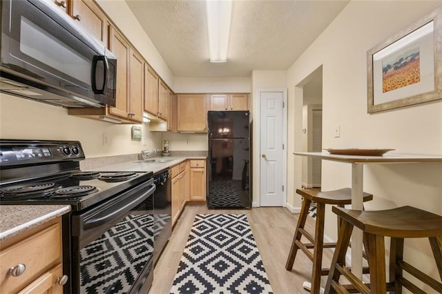kitchen featuring light countertops, light wood finished floors, black appliances, and light brown cabinets