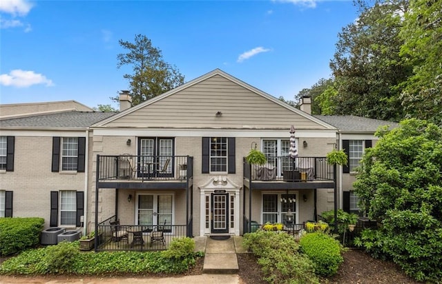 view of front of house with french doors, a chimney, brick siding, and a balcony