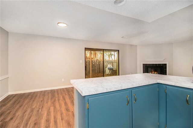 kitchen featuring a tile fireplace, dark hardwood / wood-style floors, a textured ceiling, blue cabinets, and kitchen peninsula