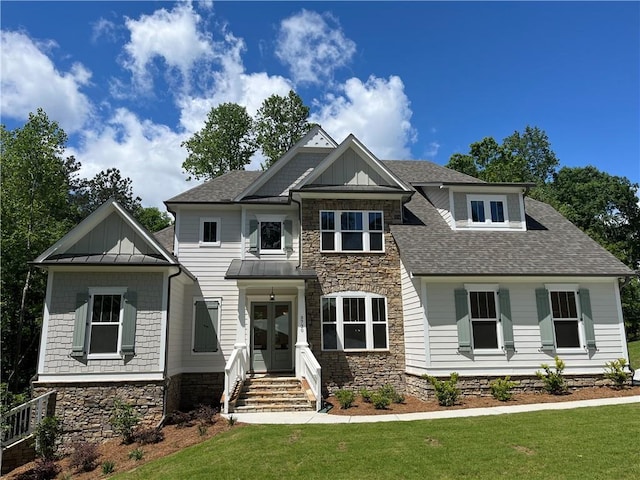 craftsman-style home featuring a standing seam roof, a front lawn, stone siding, and a shingled roof