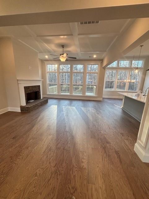 unfurnished living room featuring baseboards, ceiling fan, coffered ceiling, dark wood finished floors, and plenty of natural light