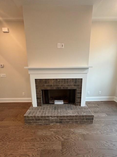 detailed view of a brick fireplace, baseboards, and wood finished floors