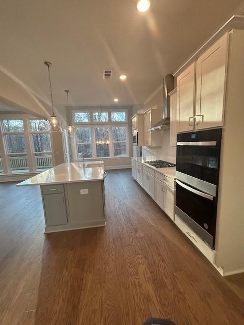 kitchen featuring wall chimney exhaust hood, double oven, dark wood finished floors, healthy amount of natural light, and recessed lighting