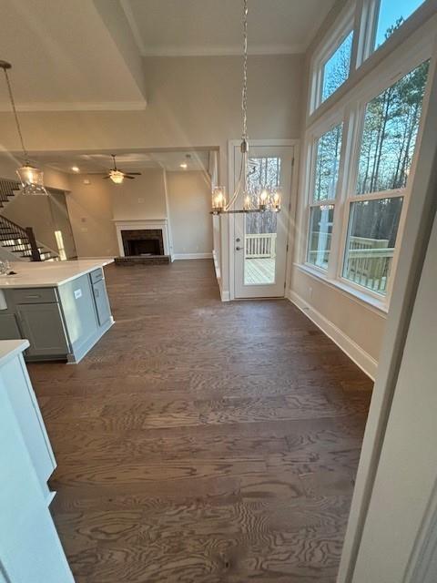 unfurnished dining area with crown molding, a chandelier, baseboards, a fireplace with raised hearth, and a ceiling fan