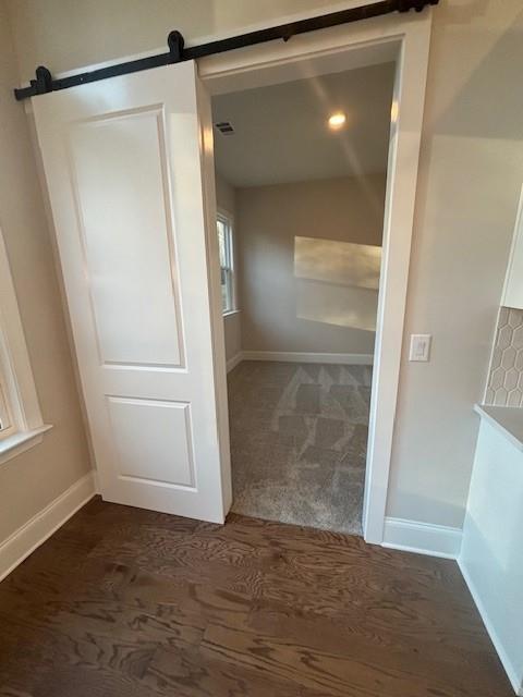 hall with a barn door, dark carpet, baseboards, and lofted ceiling