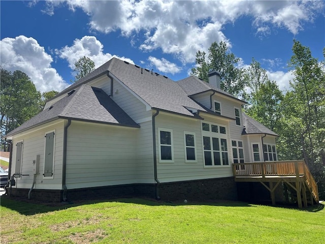 rear view of property featuring a wooden deck, a chimney, a lawn, and a shingled roof