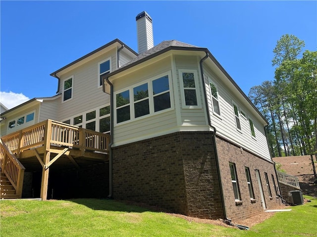 back of property with brick siding, a wooden deck, central AC, a lawn, and a chimney