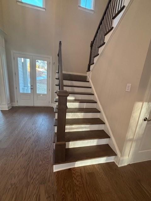 staircase featuring wood finished floors, french doors, a towering ceiling, and baseboards