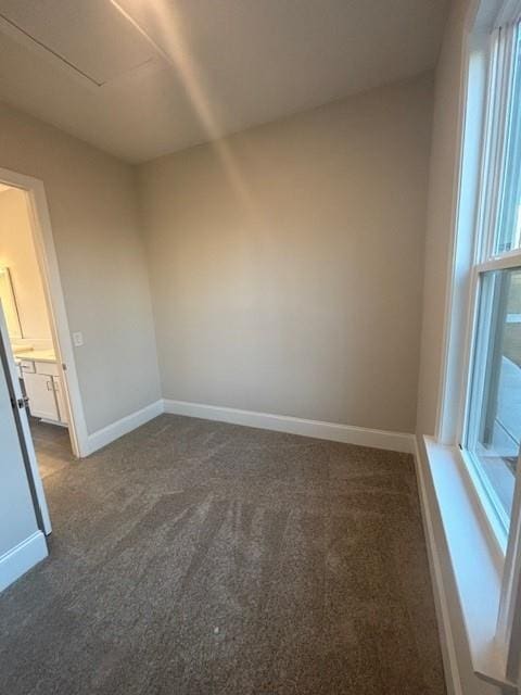 spare room featuring dark colored carpet and baseboards
