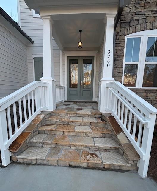 entrance to property with french doors, a porch, and stone siding