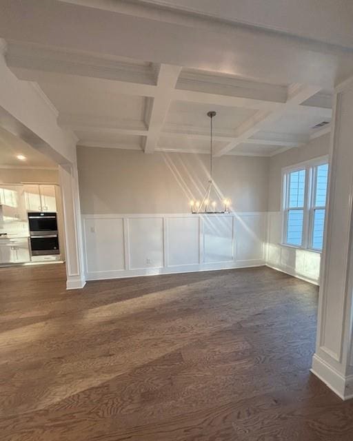 unfurnished dining area featuring a chandelier, a decorative wall, beam ceiling, coffered ceiling, and dark wood-style flooring