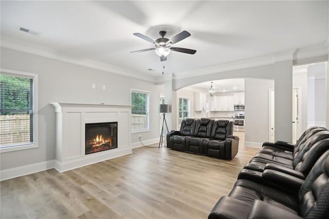 living room featuring a wealth of natural light, visible vents, crown molding, and light wood-style flooring