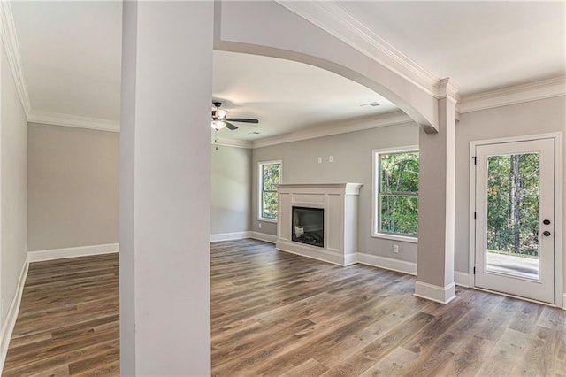 unfurnished living room with crown molding, arched walkways, wood finished floors, and a glass covered fireplace