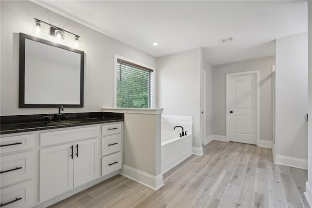 bathroom with a garden tub, visible vents, wood tiled floor, vanity, and baseboards