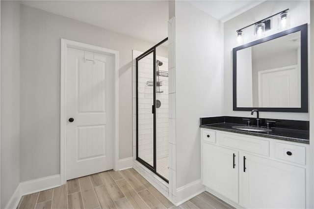 full bath featuring a stall shower, wood tiled floor, baseboards, and vanity