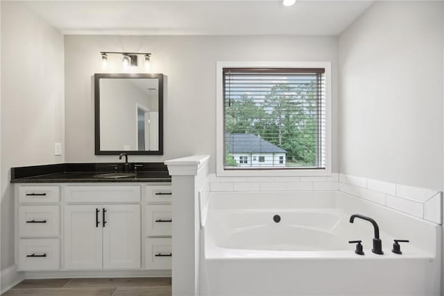 bathroom with a garden tub, wood finished floors, and vanity