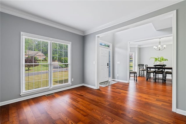 entrance foyer with a notable chandelier, baseboards, wood finished floors, visible vents, and ornamental molding