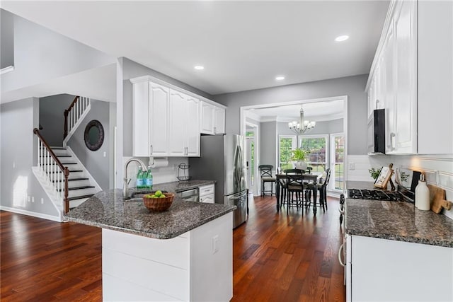 kitchen featuring white cabinets, appliances with stainless steel finishes, an inviting chandelier, a peninsula, and dark wood-style floors