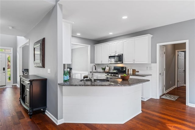 kitchen with a sink, dark wood finished floors, dark stone counters, stainless steel appliances, and white cabinetry