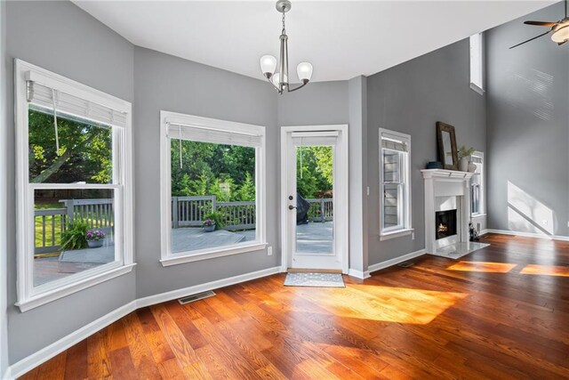 unfurnished living room with visible vents, a wealth of natural light, wood finished floors, and ceiling fan with notable chandelier