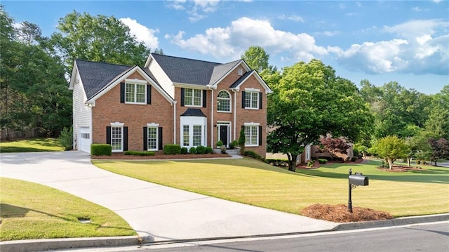 colonial house featuring brick siding, an attached garage, driveway, and a front yard