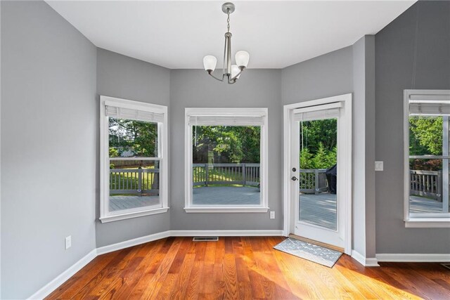 unfurnished dining area featuring wood finished floors, plenty of natural light, visible vents, and a notable chandelier