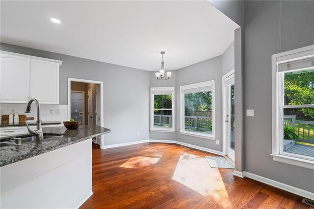 kitchen featuring an inviting chandelier, dark wood-style flooring, dark stone counters, white cabinets, and a sink