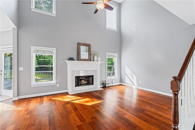 unfurnished living room featuring a ceiling fan, wood finished floors, stairway, a high ceiling, and a premium fireplace