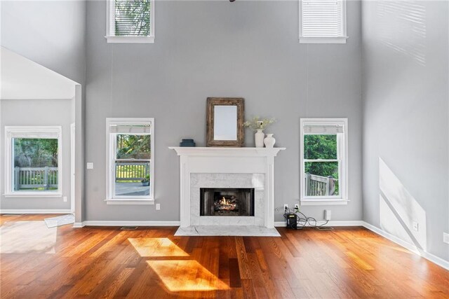 unfurnished living room featuring a premium fireplace, a high ceiling, a healthy amount of sunlight, and wood finished floors